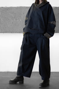 Person wearing a dark outfit with plaid accents against a plain background