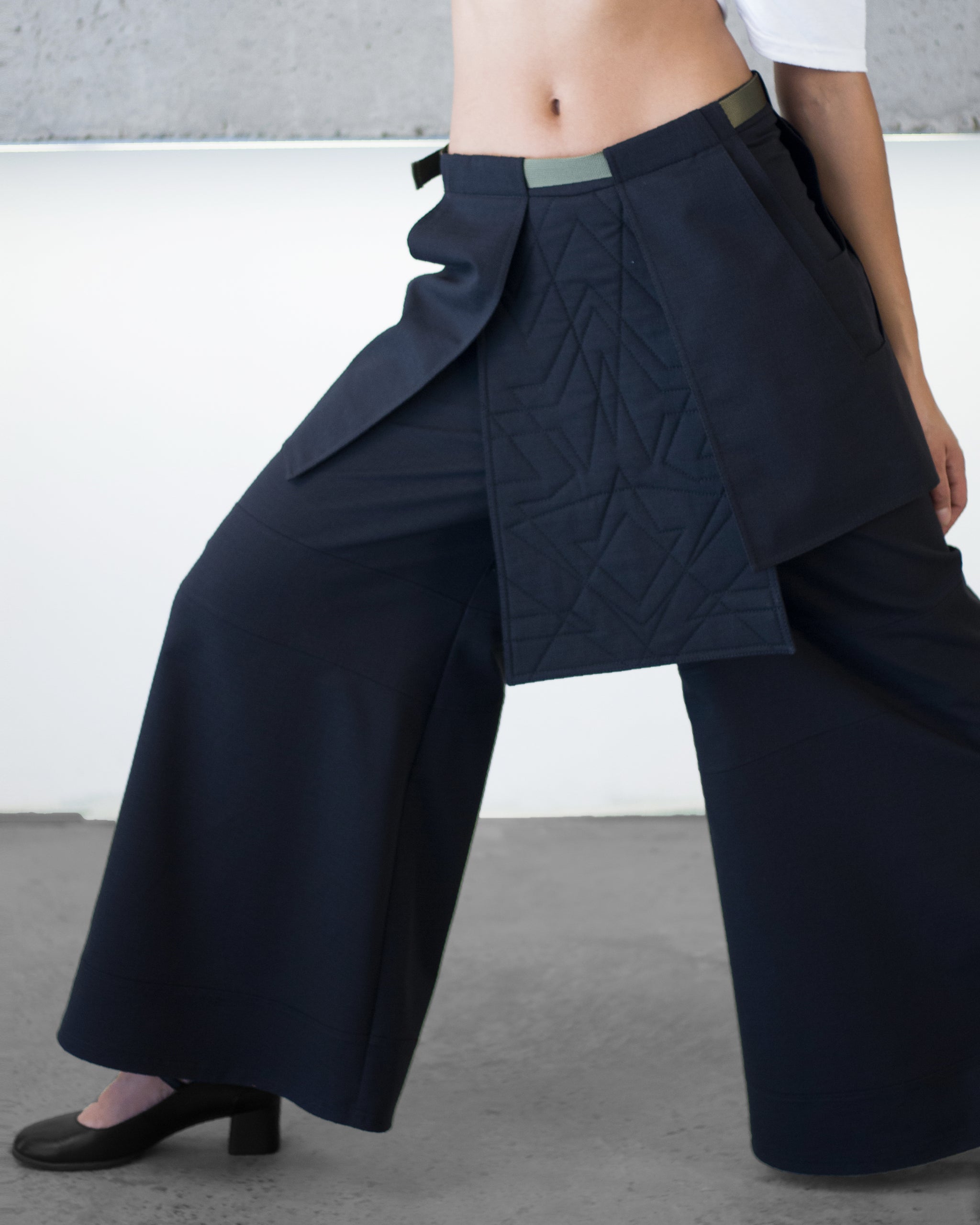 Person wearing a dark blue wide-leg pants with a quilted design on a neutral background