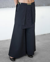 Person wearing a dark blue layered outfit with wide-leg pants against a neutral background