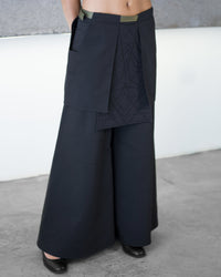 Person wearing a dark blue layered outfit with wide-leg pants against a neutral background