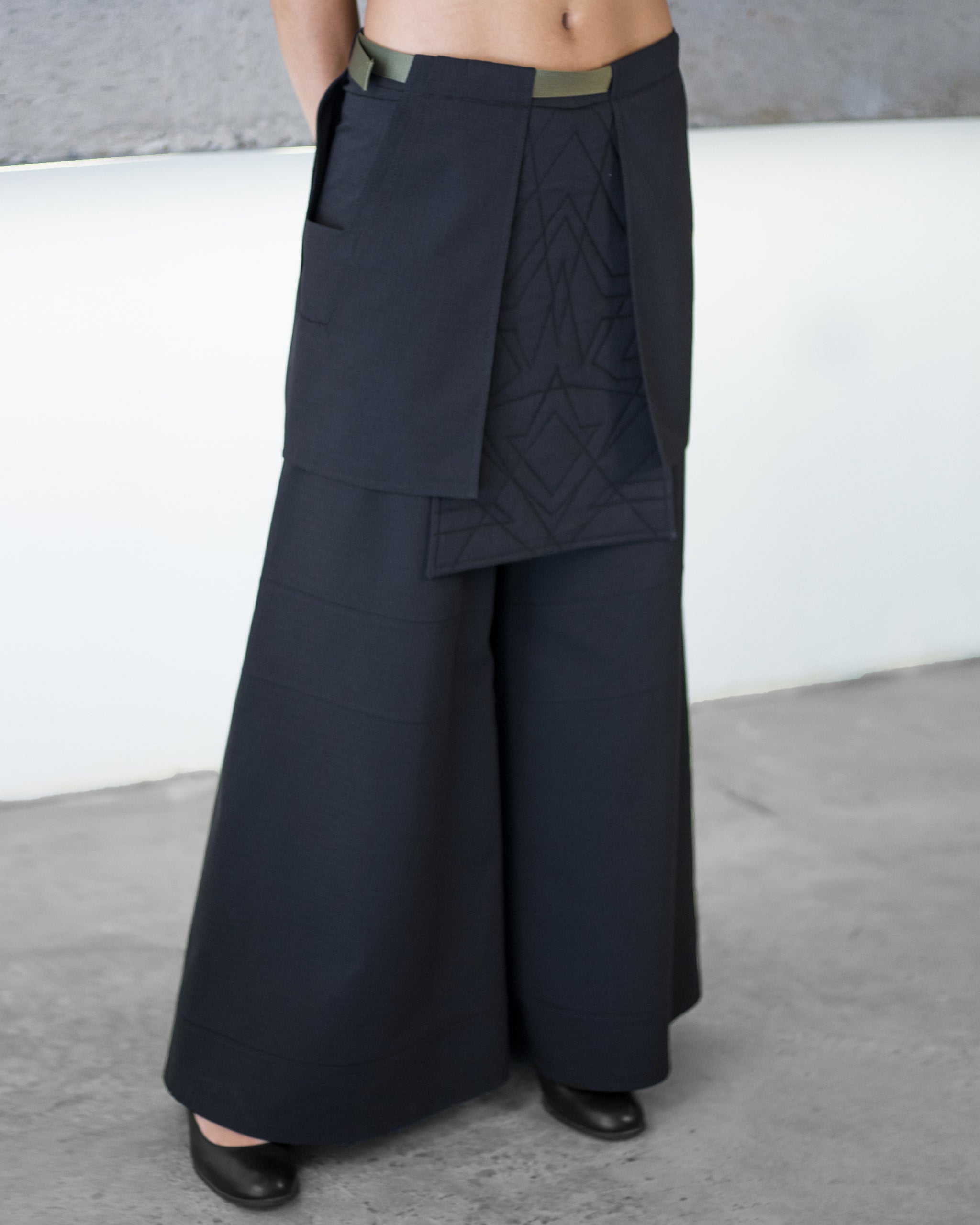 Person wearing a dark blue layered outfit with wide-leg pants against a neutral background
